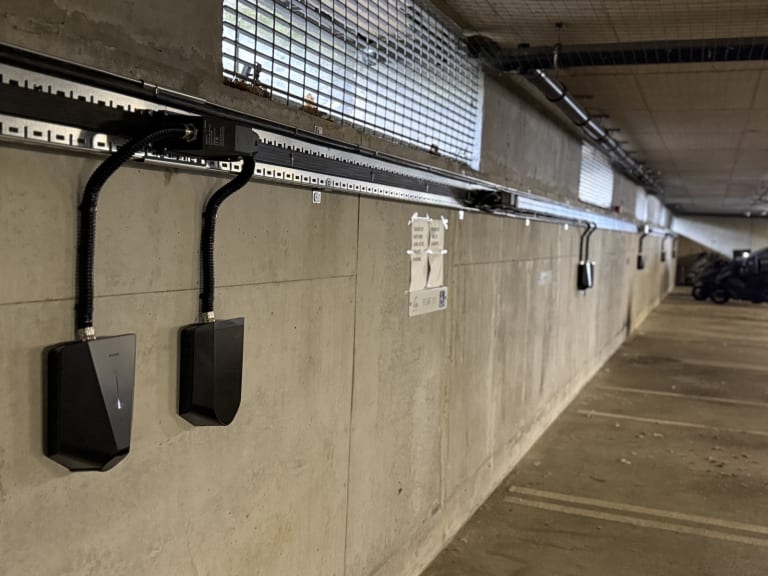Black EV chargers mounted along a concrete wall in the underground car park at Tulip Court, Alpine Place, fed from an overhead busbar running the length of the bay.